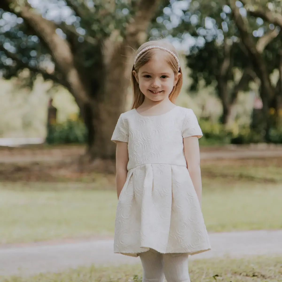 Little girl in a linen dress by an oak tree